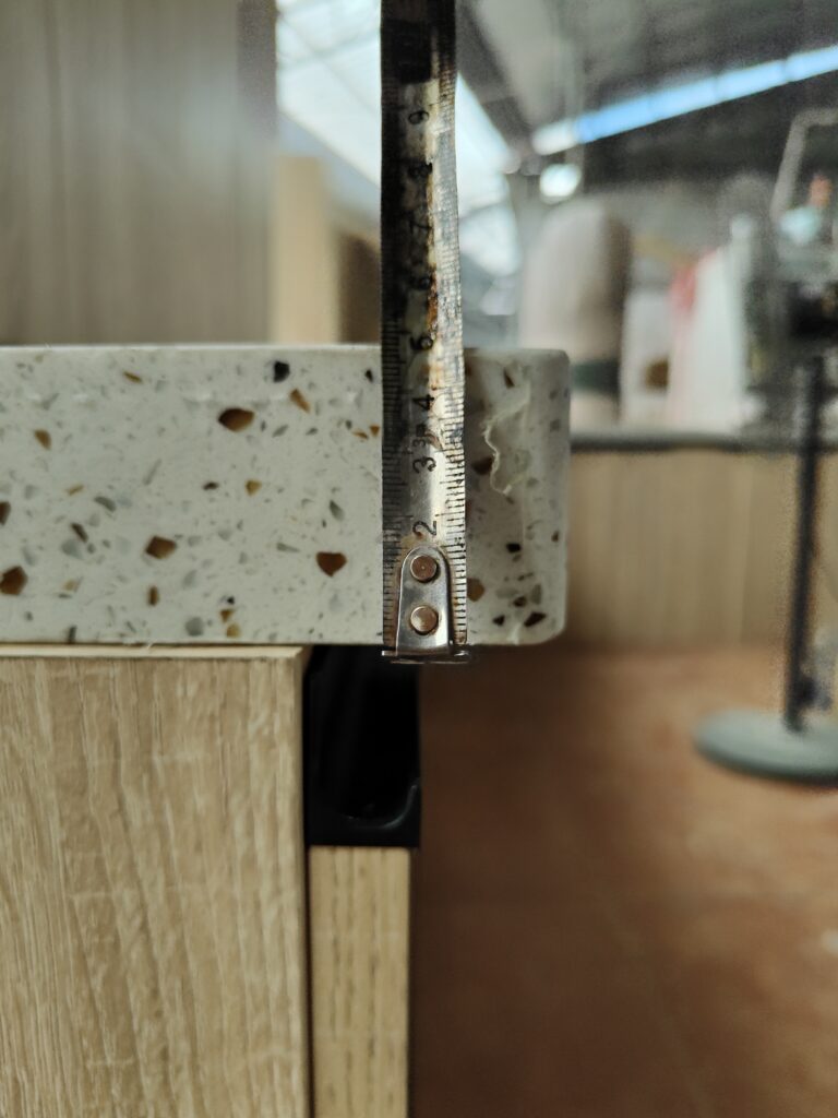QC inspector measures quartz countertop overhang dimension against French project drawing